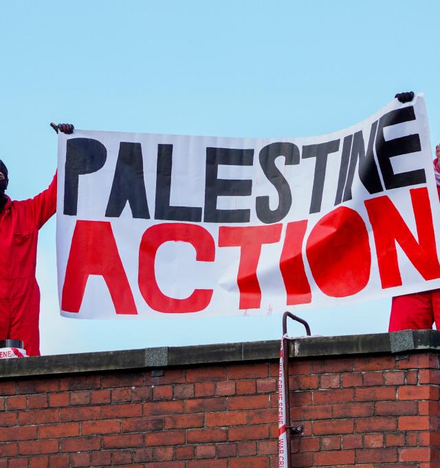 Twee mensen van Palestine Action dragen een banner bovenop het dak van een Elbit-fabriek.